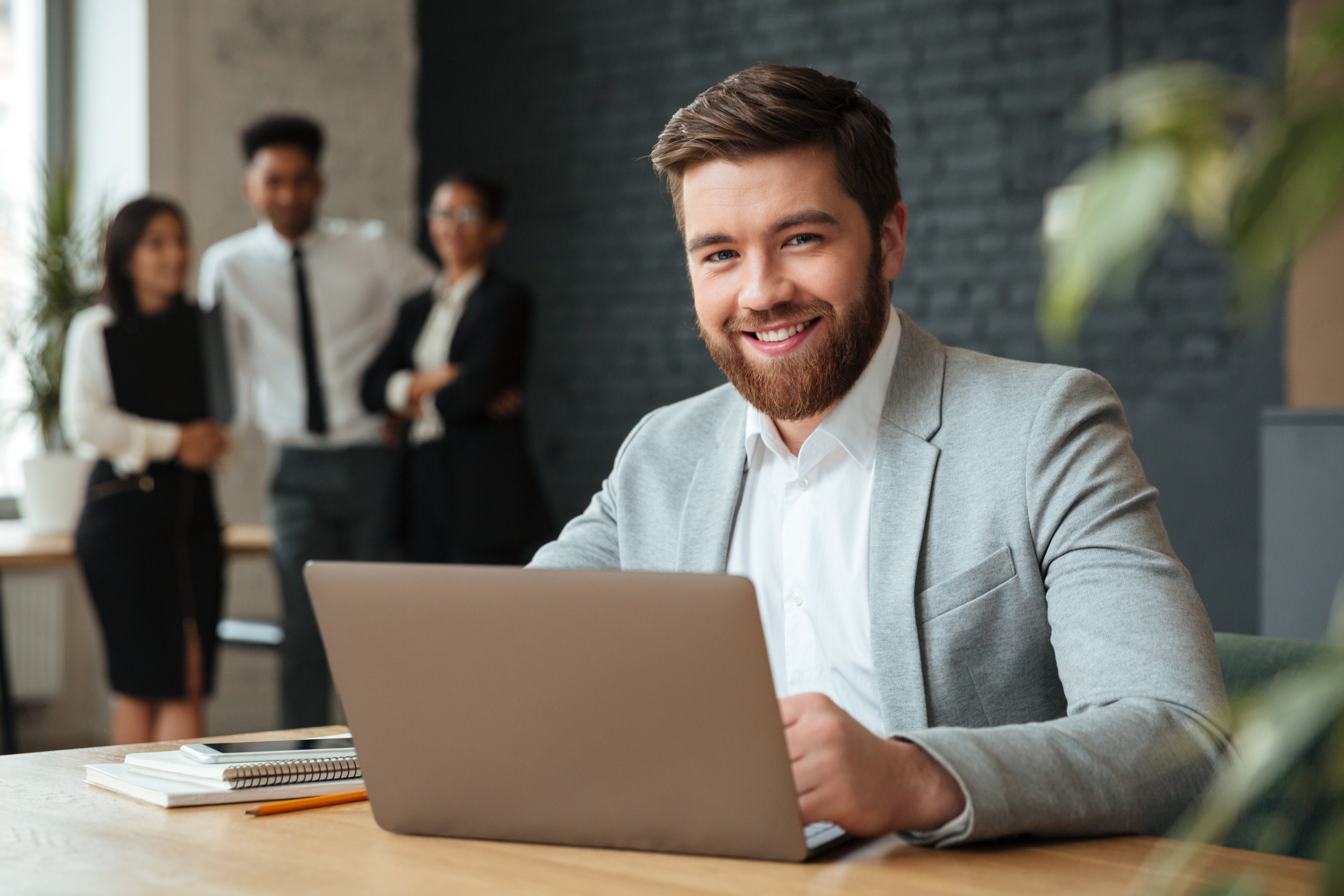 Business consultant at desk with laptop smiling with team in background